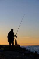 un' uomo in piedi e pesca a il kyrenia porto a il blu ora nel Cipro foto