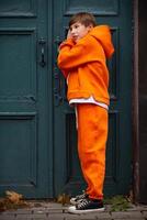 un' adolescenziale ragazzo nel un arancia completo da uomo sta a il verde porta e origliare. foto