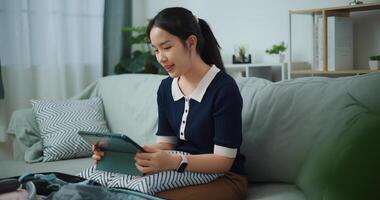 ritratto di asiatico adolescente donna seduta su divano pianificazione vacanza viaggio e ricerca informazione su digitale tavoletta, viaggio e stile di vita. foto