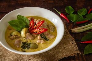 chiuso su tradizionale tailandese pollo verde curry con fresco verdura e erba nel ciotola su di legno tavolo, tailandese cibo concetto foto