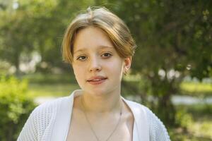 avvicinamento ritratto di un' dai capelli rossi adolescenziale ragazza nel il parco contro il fondale di fogliame. foto