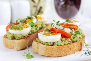 delizioso crostini con avocado, bollito uovo, pomodori e microgreen su un' bianca piatto. salutare mangiare, prima colazione. cheto dieta cibo. di moda cibo. foto