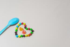 cuore sagomato caramella e Multi colorato caramella e blu cucchiaio su isolato su bianca sfondo. foto