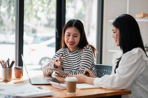 Due impegnato donne condivisione idee e Lavorando insieme su un' progetto nel un' bar, con caffè e computer portatili su il tavolo. foto