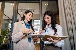 attività commerciale squadra asiatico donna Lavorando utilizzando digitale tavoletta Tech discutere finanziario mercato dati in piedi a aziendale ufficio incontro foto