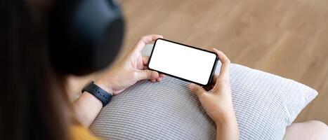 modello smartphone di un' donna Tenere mobile Telefono con vuoto bianca schermo mentre seduta ascolta per musica a casa foto