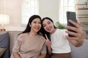 figlia adulto assunzione autoscatto utilizzando mobile Telefono con anziano madre a casa foto
