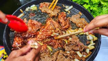 un' persona è cucinando carne nel un' padella con bastoncini foto