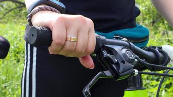 la mano della donna con l'anello sul manubrio di una mountain bike nel primo piano del parco. il motociclista si appoggia al manubrio della moto. foto