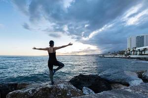 donna che pratica yoga di fronte al mare in una giornata nuvolosa foto