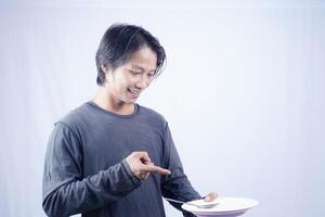 asiatico uomo puntamento in direzione vuoto piatto con contento espressione isolato bianca sfondo per caffè foto spazio. cibo menù presentazione concetto.