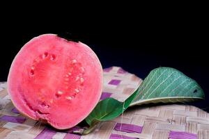 guaiava isolato. guaiava frutta con rosso carne con giallastro verde pelle e le foglie isolato su un' nero sfondo con intrecciata bambù come un' base. foto