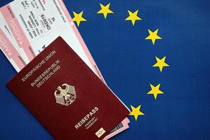 rosso Tedesco passaporto di europeo unione e le compagnie aeree Biglietti su blu bandiera sfondo vicino su foto