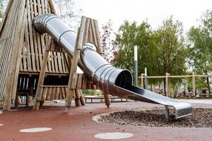 un' metallo diapositiva su il terreno di gioco, un' moderno terreno di gioco per bambini, un' gli sport complesso su il strada, un' di legno scalatore, un la zona per a piedi con bambini. foto