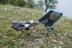 turista utensili per escursioni a piedi siamo su il tavolo, compatto attrezzatura per all'aperto ricreazione, campeggio nel il foresta, un' posto per rilassare nel il montagne, un' pieghevole sedia. foto