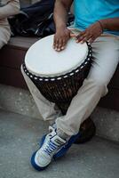 un' nero tipo estratti il suoni di un' tamburo con un' punch, un' strada musicista batteria tra il folla, un africano giochi il ritmi di il tribù. foto