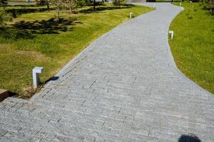 un' pietra strada è pavimentata con ciottoli, un' strada di pietra mattoni, un' città parco per a passeggio, un' pedone strada, un' falciato prato. foto