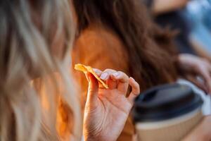 un' ragazza mangia spuntini al di fuori potabile caffè, un' donna di mano detiene un' pezzo di biscotti, secco Mango è bloccato nel il ragazze dita, prima colazione fuori, veloce cibo. foto