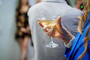 un' donna di mano detiene un' bicchiere di Champagne, un' scintillante bevanda versato in un' bicchiere, trasparente bicchiere, un' banchetto, avvicinamento, un' festa con gli amici. foto