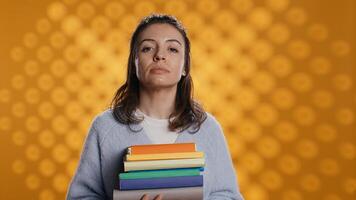 ritratto di ottimista donna Tenere mucchio di libri, godendo lettura passatempo per divertimento scopi. radiante topo di biblioteca con pila di romanzi nel braccia godendo tempo libero volta, studio sfondo, telecamera B foto