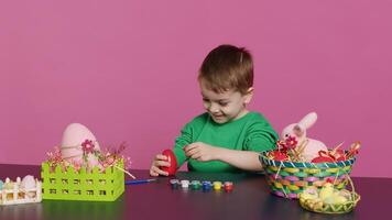 giovane bambino piccolo messa a fuoco su decorazione Pasqua uova con francobolli e acquerello dipingere, preparazione fatto a mano ornamenti per primavera vacanza festa. piccolo carino ragazzo colorazione decorazioni. telecamera un. foto