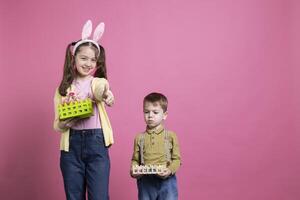 gioioso fratelli sensazione contento festeggiare Pasqua vacanza e primavera volta, poco ragazza dando pollici su su telecamera. fratello e sorella mostrando cesti pieno con dipinto uova e decorazioni. foto