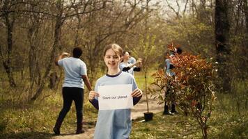 ritratto di dolce ragazza con Salva nostro pianeta manifesto contro inquinamento e illegale dumping, il volontariato per ristabilire e conserva natura nel il foresta. poco bambino Spettacoli consapevolezza cartello. telecamera b. foto