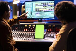 artista e suono ingegnere Lavorando con schermo verde Schermo su tavoletta, miscelazione e mastering brani con Audio consolle e digitale Software. musicisti squadra la modifica musica, motorizzato fader. foto
