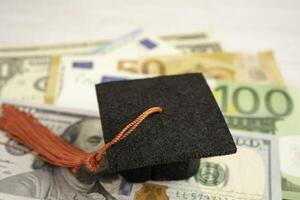 cappello di divario di laurea su banconote in euro e dollari americani, concetto di insegnamento della tassa di studio dell'istruzione. foto