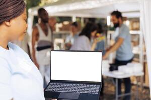 dettagliato Immagine mostrando africano americano femmina volontario trasporto il computer portatile con isolato copyspace Schermo per personalizzazione. nero donna Tenere minicomputer con bianca schermo modello modello. foto