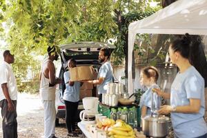 Immagine in mostra un all'aperto senza scopo di lucro cibo guidare programma per supporto il povero bisognoso e senza casa le persone. giovane multietnico volontari fornire donazione scatole per il svantaggiato. foto