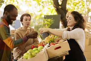 contento multiculturale coppia degustazione bio biologico produrre a agricoltori mercato, acquisto localmente cresciuto frutta e verdure. allegro nero uomo ricevente fetta di Mela a partire dal amichevole femmina venditore. foto