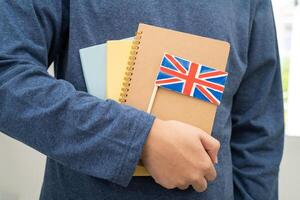 imparare inglese linguaggio, asiatico adolescenziale alunno hold libro con bandiera nel corso a scuola. foto