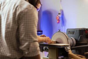 fabbricante modellare di legno ciotola su disco levigatrice nel assemblaggio negozio aiutante di collaboratore. la lavorazione del legno specialista Lavorando nel falegnameria Il prossimo per apprendista, guida legna contro macinazione macchina rotante disco foto