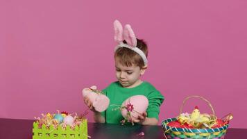 piccolo lieta bambino presentazione nascosto fatto a mano ornamenti creato nel preparazione di Pasqua vacanza celebrazione. giovane ragazzo con coniglietto orecchie mostrando dipinto decorazioni, un' coniglio e un uovo. telecamera un. foto