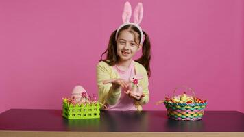 giovane scolara soffiaggio aria baci nel davanti di telecamera mentre lei crea festivo bello accordi su ripieno coniglio giocattolo. allegro giovane bambino essere eccitato di Pasqua celebrazione. telecamera b. foto