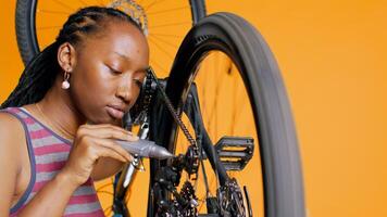 bipoc tecnico utilizzando specializzato colla per riparazione rotto bicicletta catena, arancia studio sfondo. professionale l'applicazione adesivo su bicicletta componenti durante Manutenzione processi, vicino su sparo, telecamera B foto