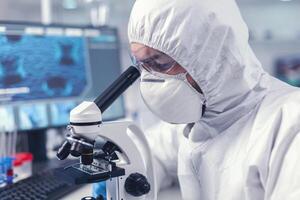 medico sviluppando vaccino utilizzando microscopio nel moderno laboratorio. virolog nel tuta durante coronavirus scoppio conduzione assistenza sanitaria scientifico analisi. foto