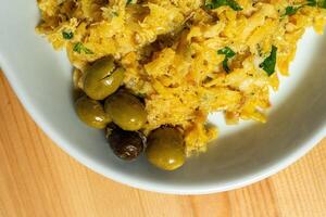 bacalhau un' reggiseni, un' tradizionale portoghese piatto, servito su un' bianca piatto nel un' ristorante ambientazione. il triturati merluzzo è misto con uova, croccante patate, prezzemolo, e nero olive. foto