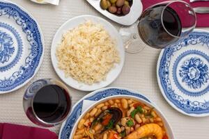 un' piatto di frutti di mare feijoada con Riso, guarnito con gamberetto e vongole, si siede su un' ristorante tavolo. a fianco siamo alentejo formaggio e un' bicchiere di rosso vino, evocando un' caldo portoghese cenare Esperienza. foto