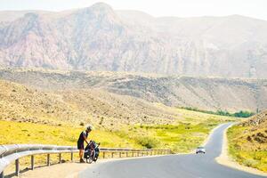 uomo In piedi di turismo bicicletta nel montagne su lato di strada imballare avere rompere tempo riposo. assolo viaggio viaggio con bicicletta borse. lungo termine viaggio in giro il mondo foto