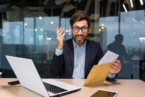 ritratto di contento maturo investitore uomo d'affari nel ufficio, uomo guardare a telecamera e scioccato contento e sorridente, capo apertura Busta con bene notizia notifica. foto