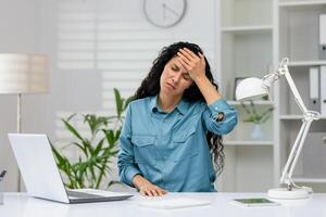 frustrato professionale femmina sperimentare fatica e mal di testa mentre Lavorando su un' il computer portatile nel un' moderno ufficio ambientazione. foto