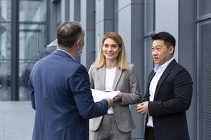 internazionale attività commerciale squadra incontro maturo uomo, caucasico donna, asiatico dipendente comunicare . gruppo di imprenditori nel formale tute discutere un' progetto documento vicino ufficio centro su strada foto