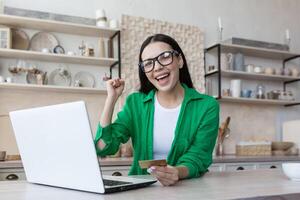 felicissimo del Millennio ragazza sedersi a tavolo a casa Guarda a il computer portatile schermo sentire euforico vincente foto