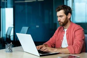 grave concentrato pensiero uomo d'affari Lavorando con il computer portatile dentro ufficio a posto di lavoro, uomo digitando su tastiera del computer, preparazione in linea presentazione e finanziario contabilità rapporto. foto