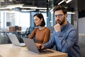 pensieroso unshaved tipo nel denim camicia riposo testa su mano mentre guardare a telecamera Il prossimo per femmina collega. Due digitale progettisti sviluppando nuovo creativo strategia per sociale media per marketing squadra. foto