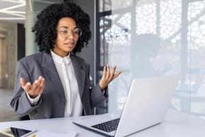 giovane riuscito afroamericano donna d'affari comunica attraverso chiamata con clienti, partner, conduce attività commerciale addestramento. seduta nel il ufficio a il il computer portatile. foto