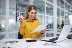 soddisfatto con finanziario risultati e reddito, donna d'affari capo a posto di lavoro celebra vittoria, finanziario donna detiene rapporto, account, contrarre nel mani, con gioia celebra trionfo dentro ufficio. foto