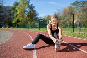 un' determinato donna tratti sua gamba muscoli prima un' correre su un' traccia campo, illustrare fitness e preparazione. foto